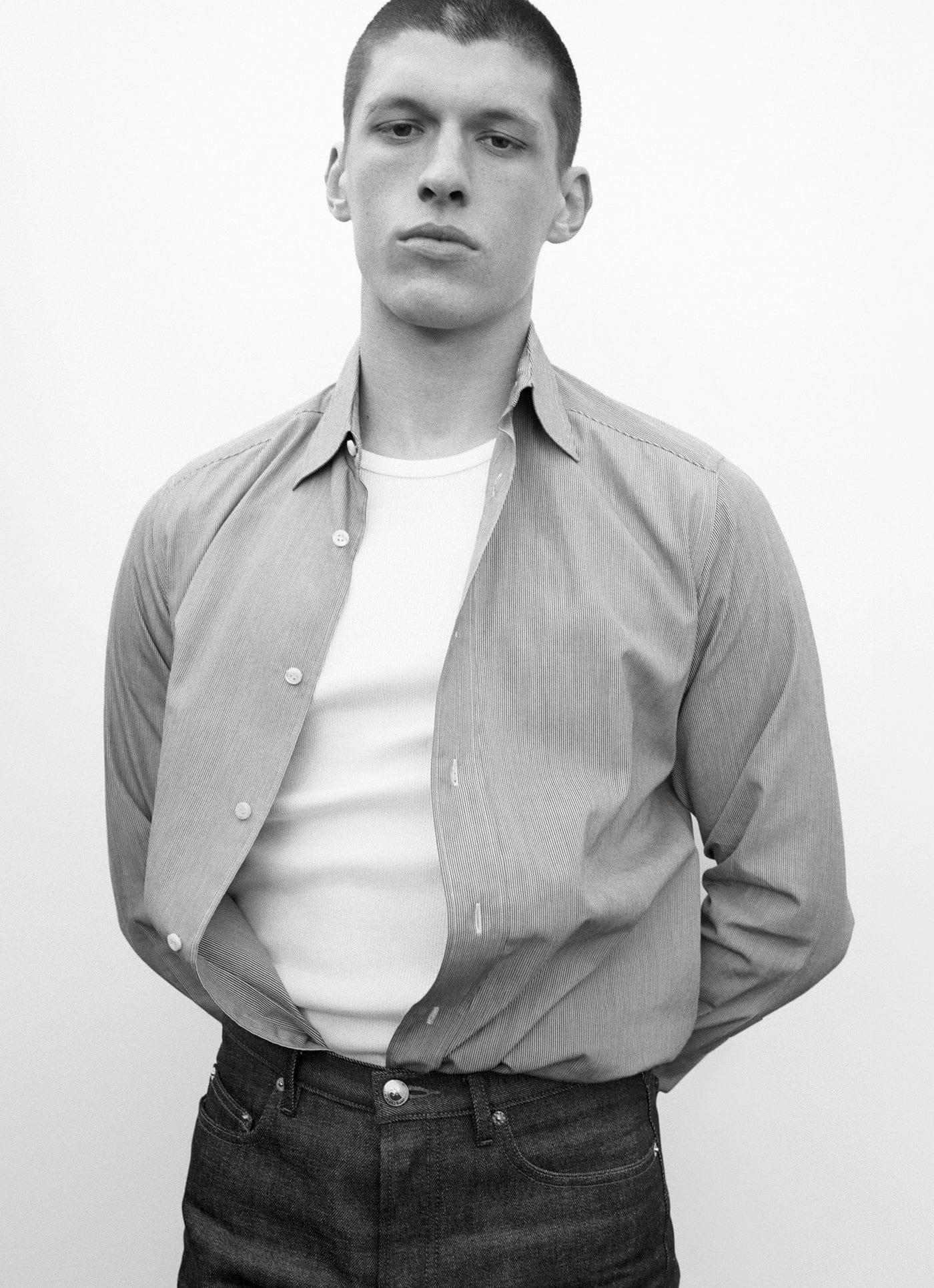 Homme en chemise grise ouverte sur un tee-shirt blanc et jean foncé A.P.C., photographié en noir et blanc