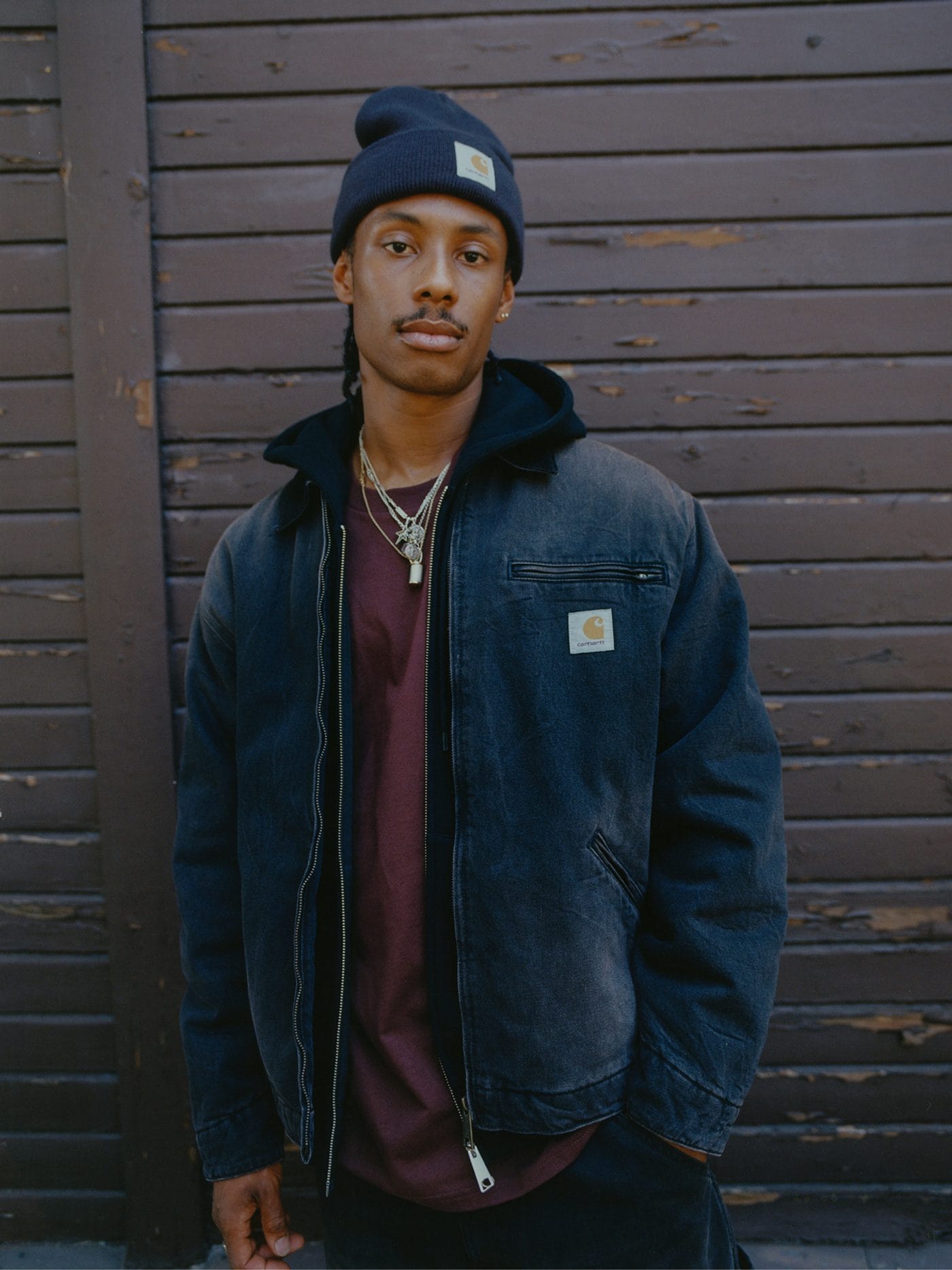 Homme en bonnet et veste sombre Carhartt WIP portés sur un sweat à capuche bordeaux