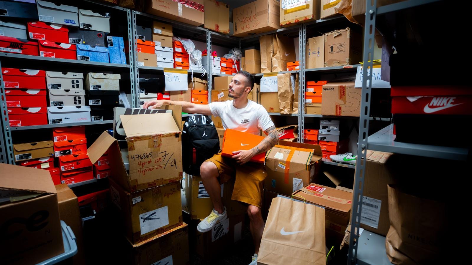 Vendeur assis dans une réserve entourée de boîtes de chaussures empilées